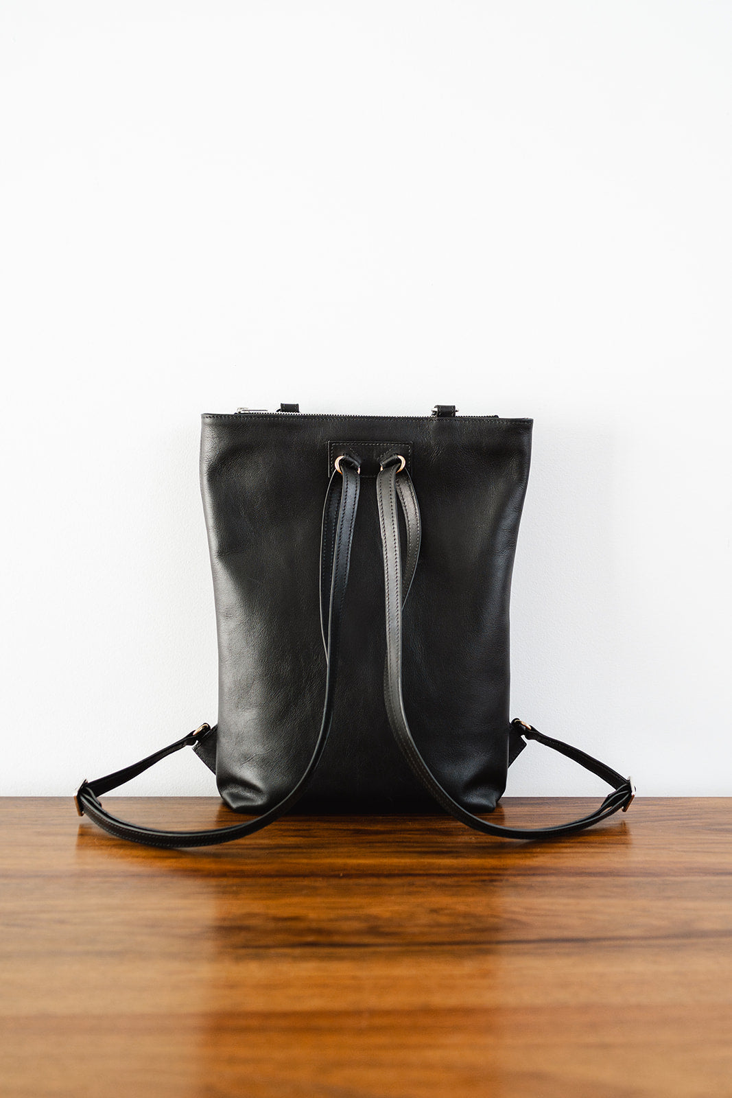 Rear view of The Backpack by Ella Jackson Australia – black leather backpack on timber table, minimalist setting.