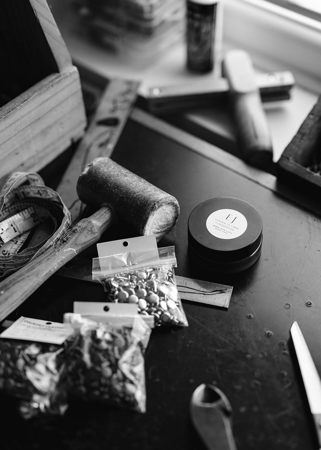 Ella Jackson Natural Leather Conditioner — jar on a leatherwork bench surrounded by tools and brass hardware