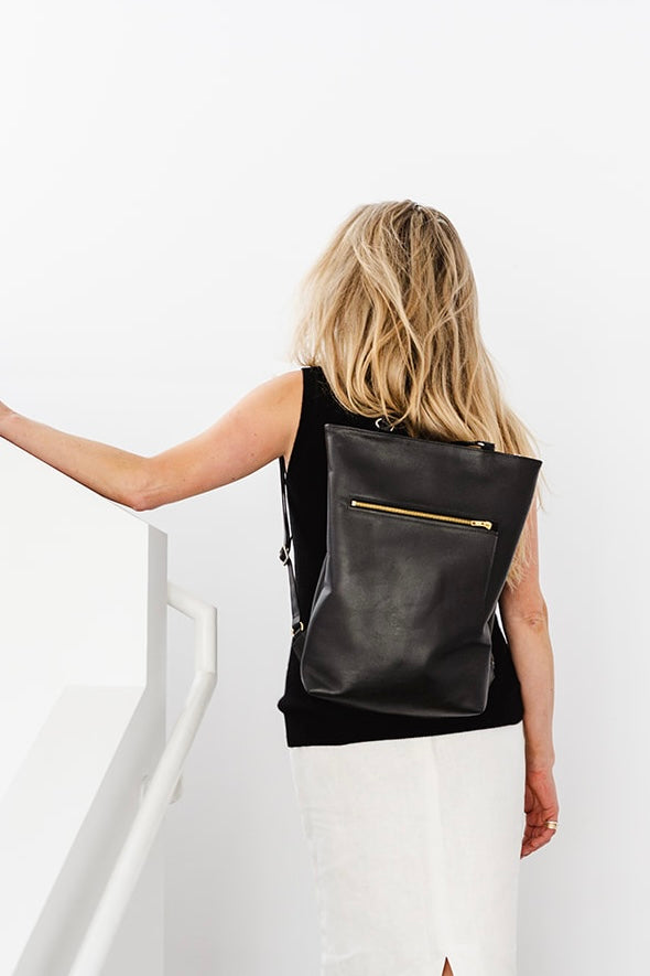 Woman wearing The Backpack by Ella Jackson Australia – minimalist black leather backpack, photographed mid-staircase.