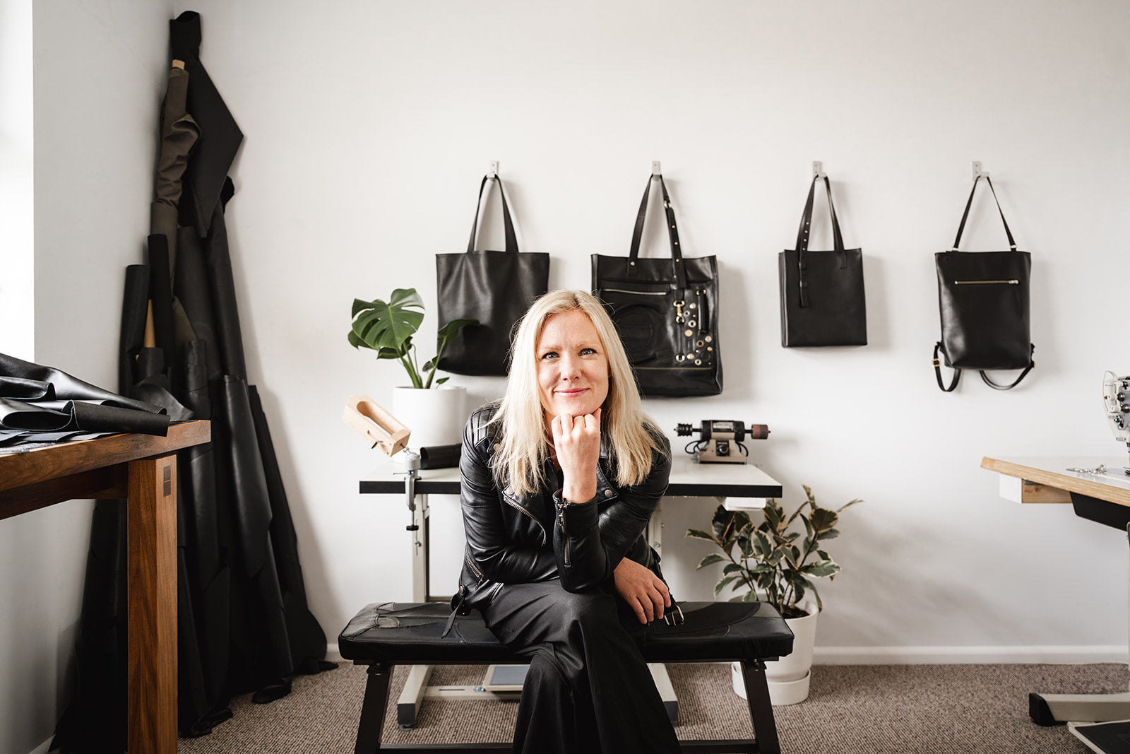 Ella Jackson seated in her Tasmanian leather studio – handmade leather bags displayed on the wall.