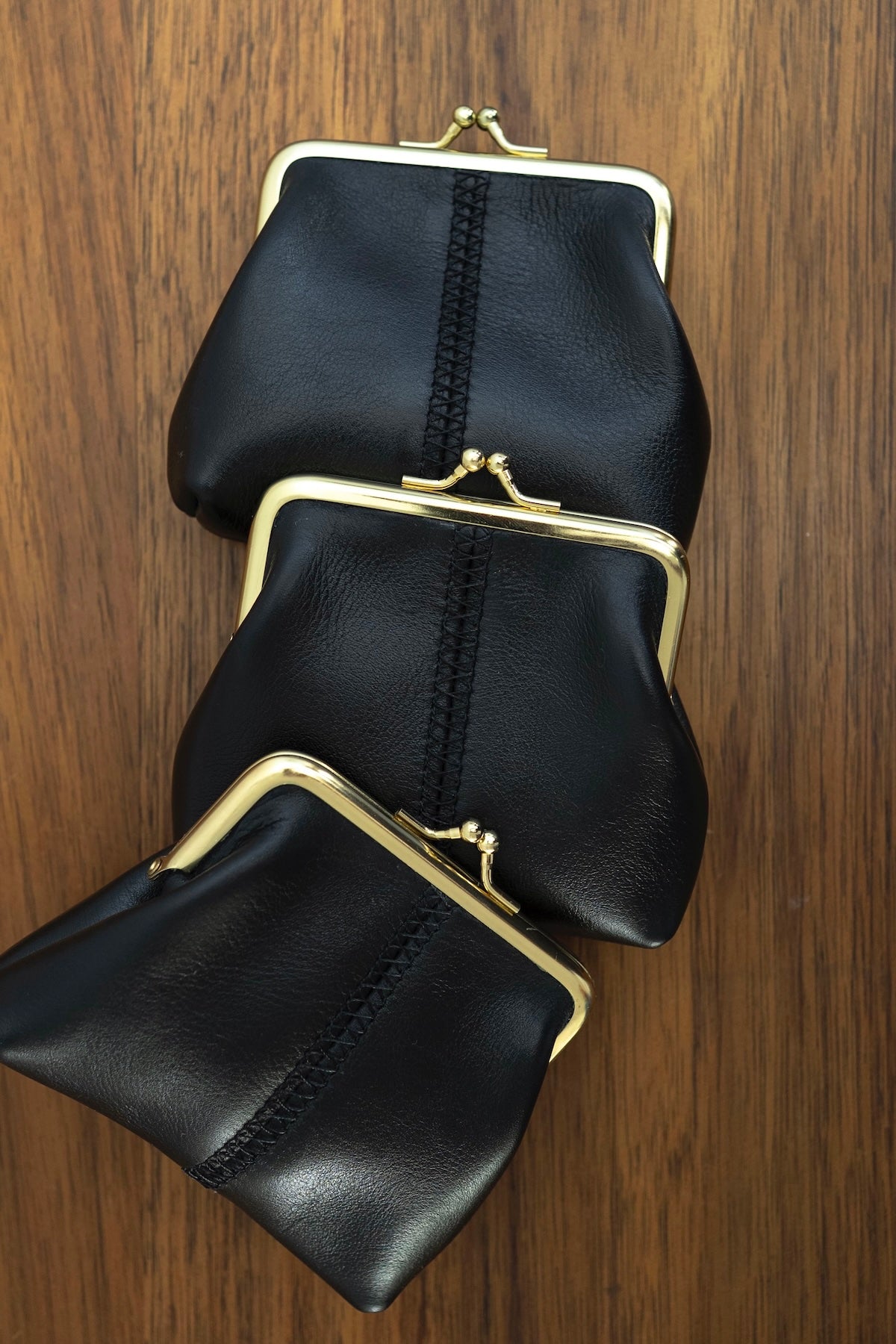 The Frame Purse by Ella Jackson Australia — three black leather frame purses stacked diagonally on timber surface
