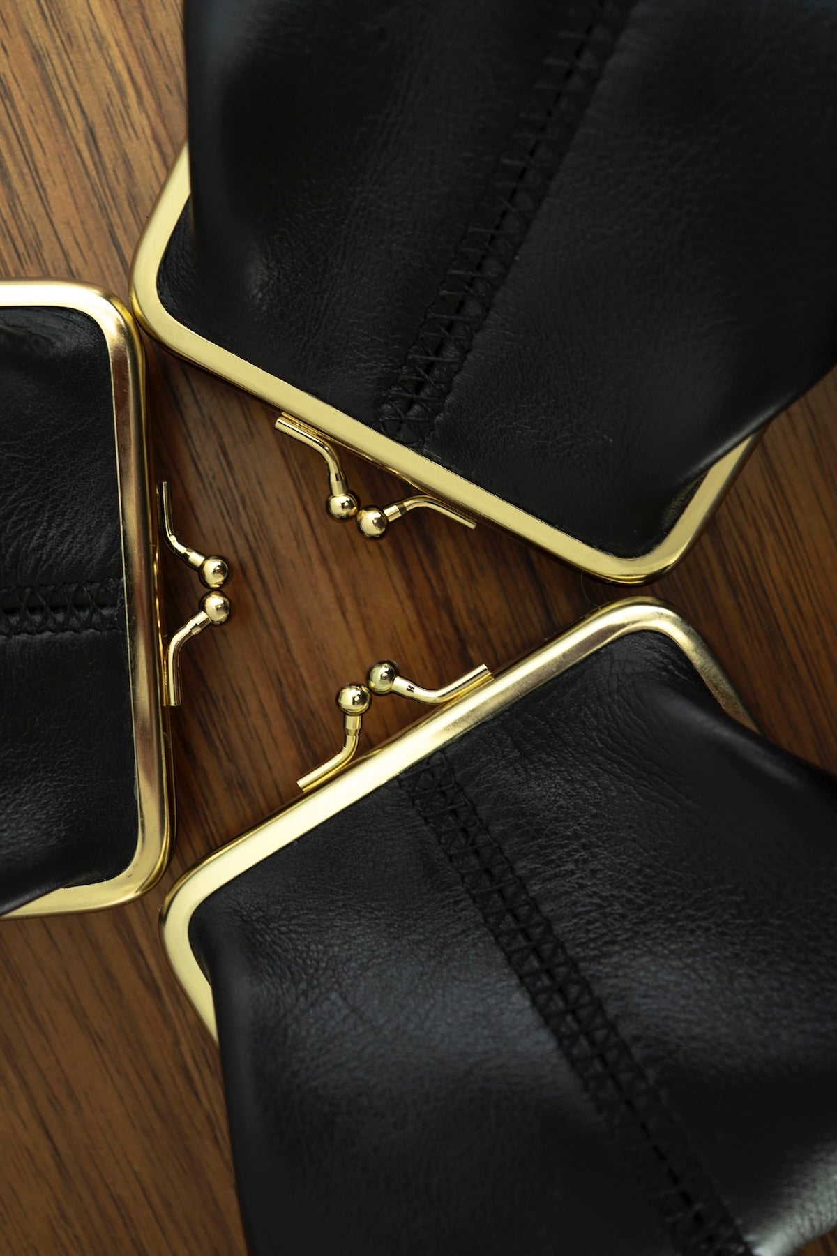 The Frame Purse by Ella Jackson Australia — three black leather frame purses with gold clasps arranged in a triangle on timber, showcasing stitching and metalwork