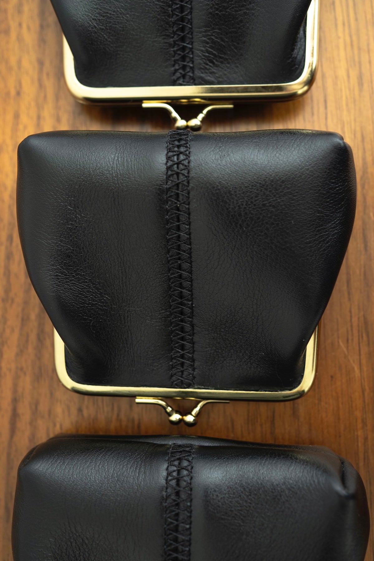 The Frame Purse by Ella Jackson Australia — top-down view of three black leather frame purses aligned vertically with signature centre stitching and gold hardware