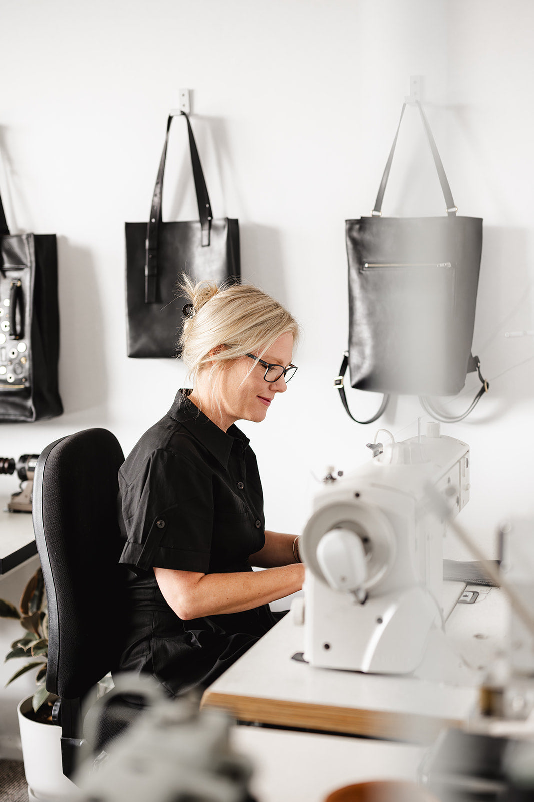 Ella Jackson working at her sewing machine in STUDIO Ella Jackson, Bellerive, Tasmania. Handmade leather bags hang on the wall behind her in the working studio