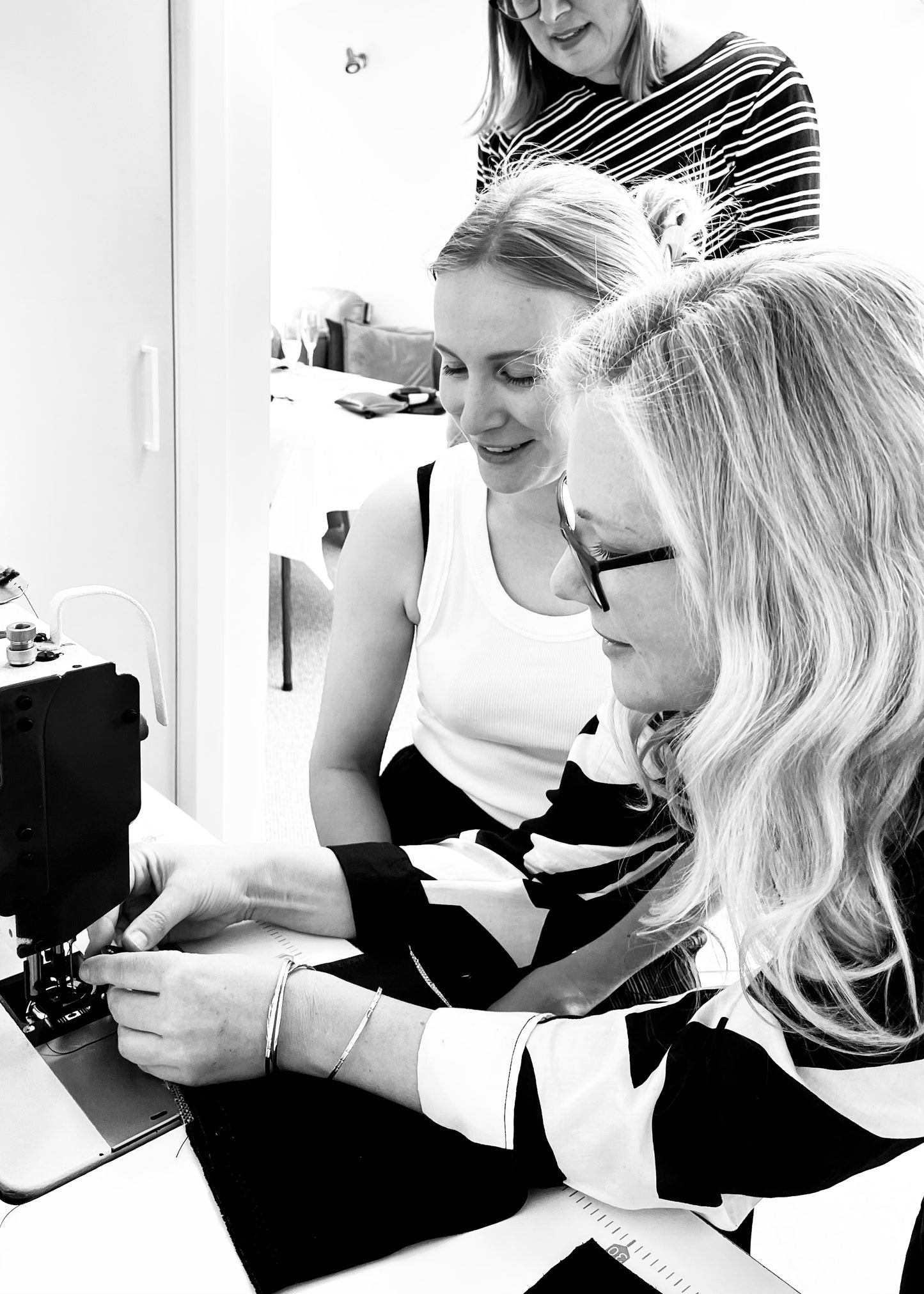 Participants concentrating at a sewing machine during a leather tote bag workshop, working together to carefully stitch leather pieces with precision and focus