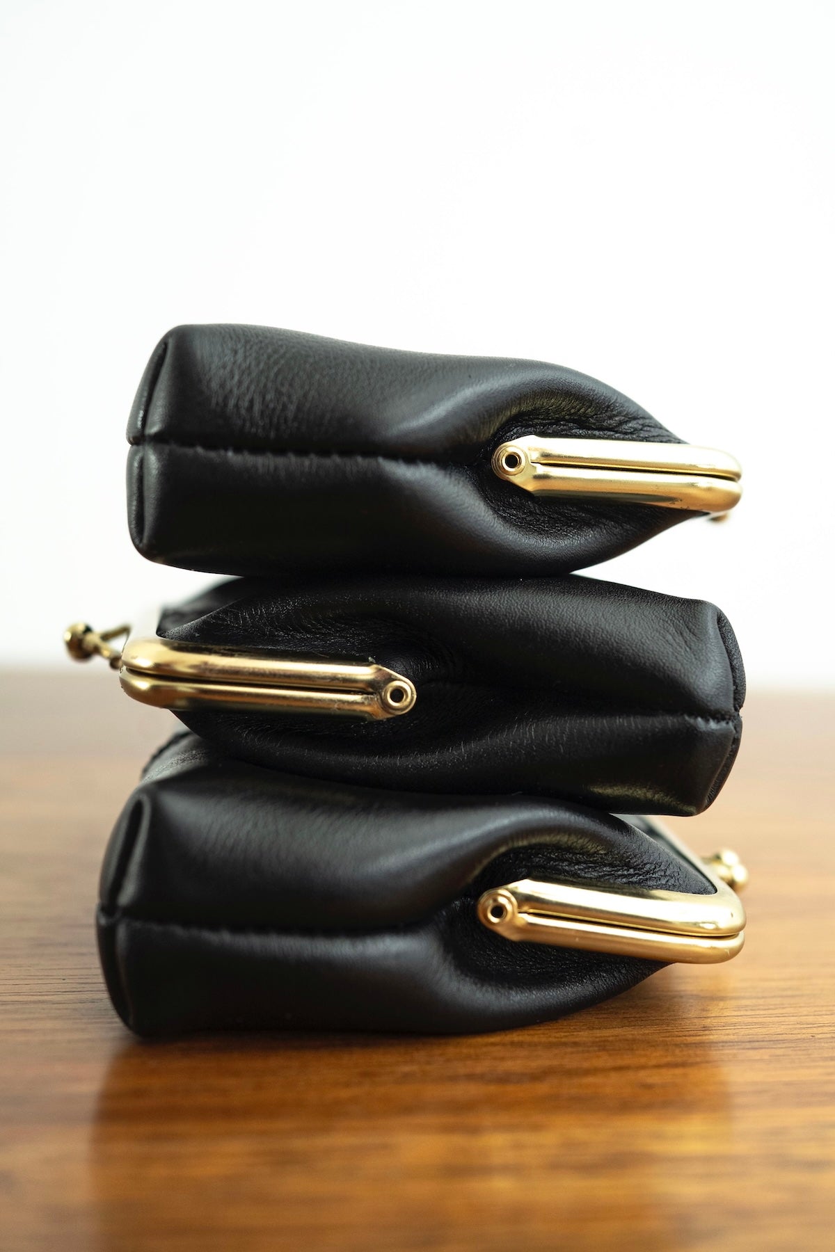 The Frame Purse by Ella Jackson Australia — stacked side view of three black leather purses showing gold clasp hardware and soft structure