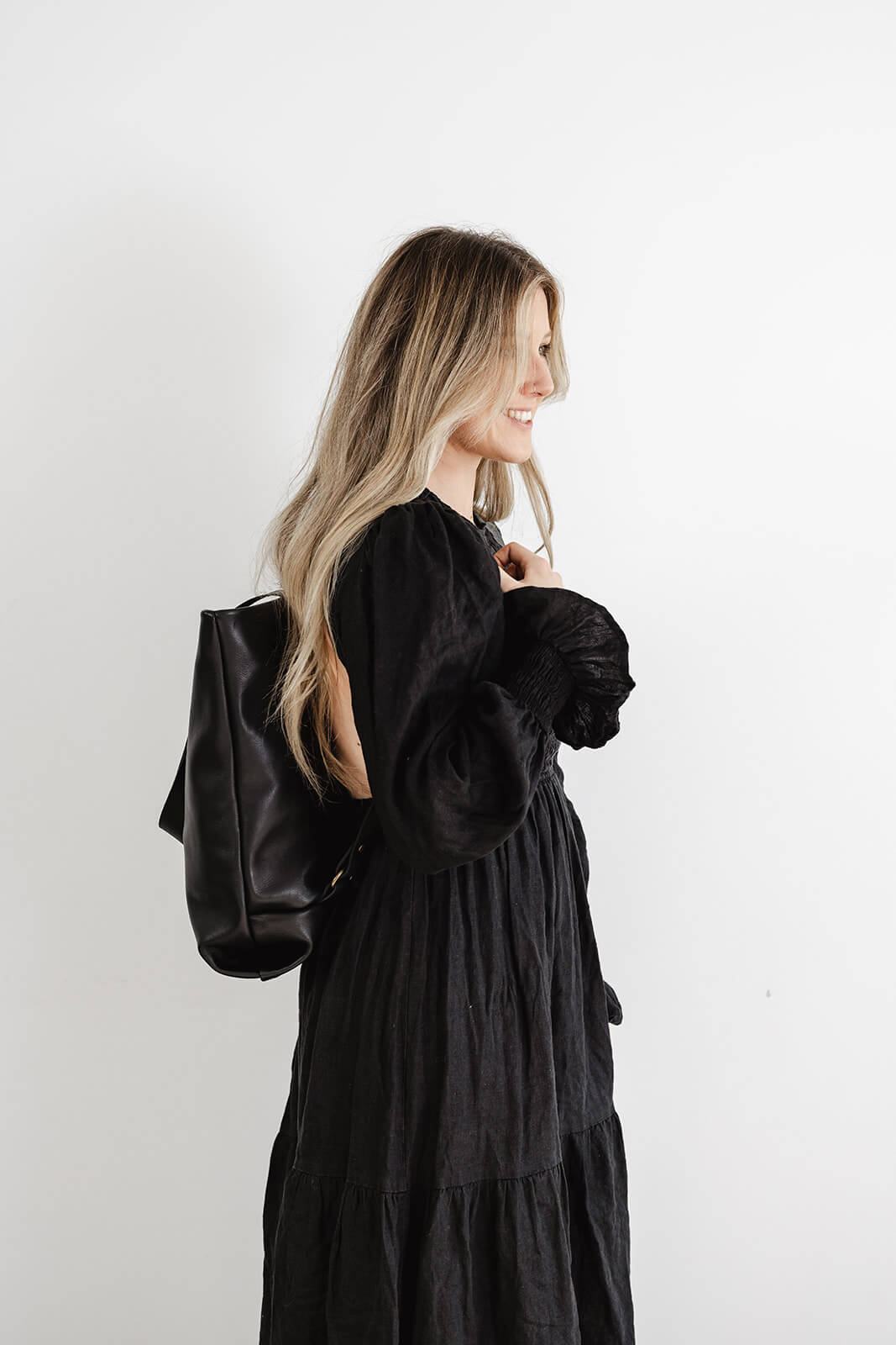 Woman with long flowing hair and wearing black dress. Profile photo showing profile of Ella Jackson Leather Backpack & Tote in Black