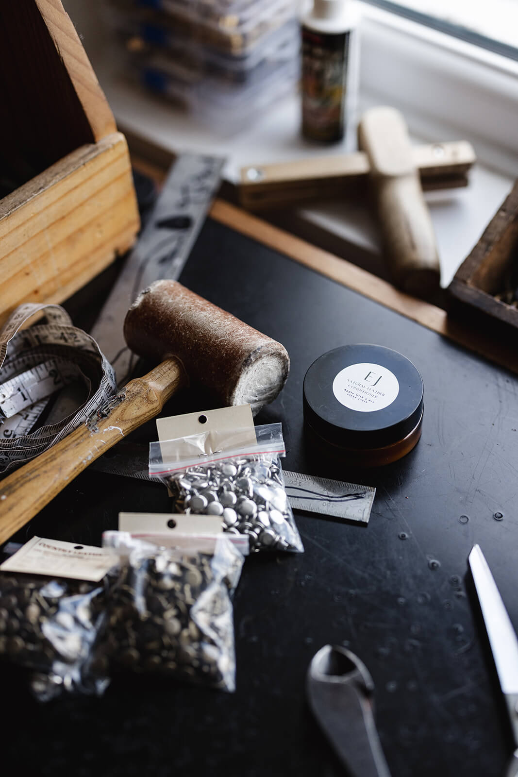 Work bench with various tools including mallet, rivet, tool box, strap cutter and a pot of Ella Jackson Natural Leather Conditioner