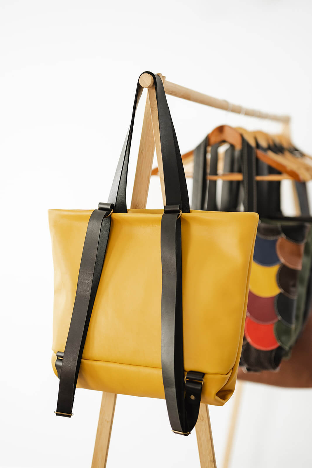 Yellow Leather Backpack & Tote in Ella Jackson brand hanging on timber clothes rack backwards as a tote and showing black leather backpack and tote straps. Colourful leather backpack hanging behind