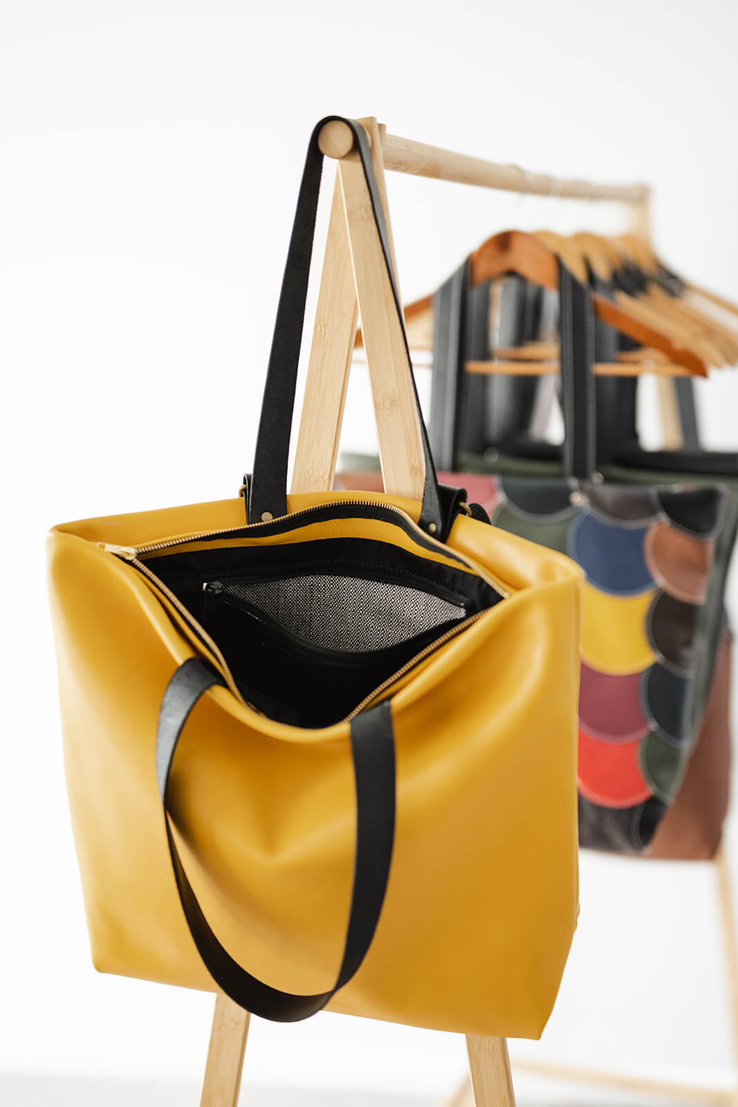 Yellow Leather Backpack & Tote in Ella Jackson brand hanging on timber clothes rack as a tote and showing open bag, straps, gold zip and internal pocket with white and black commercial fabric. Colourful leather backpack hanging behind