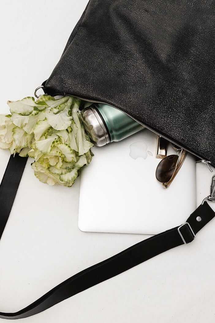 Open grey carryall bag with black strap, silver hardware, and black and silver zip. Photo shows what the bag holds...laptop, a bunch of flowers, water bottle and sunglasses. White background