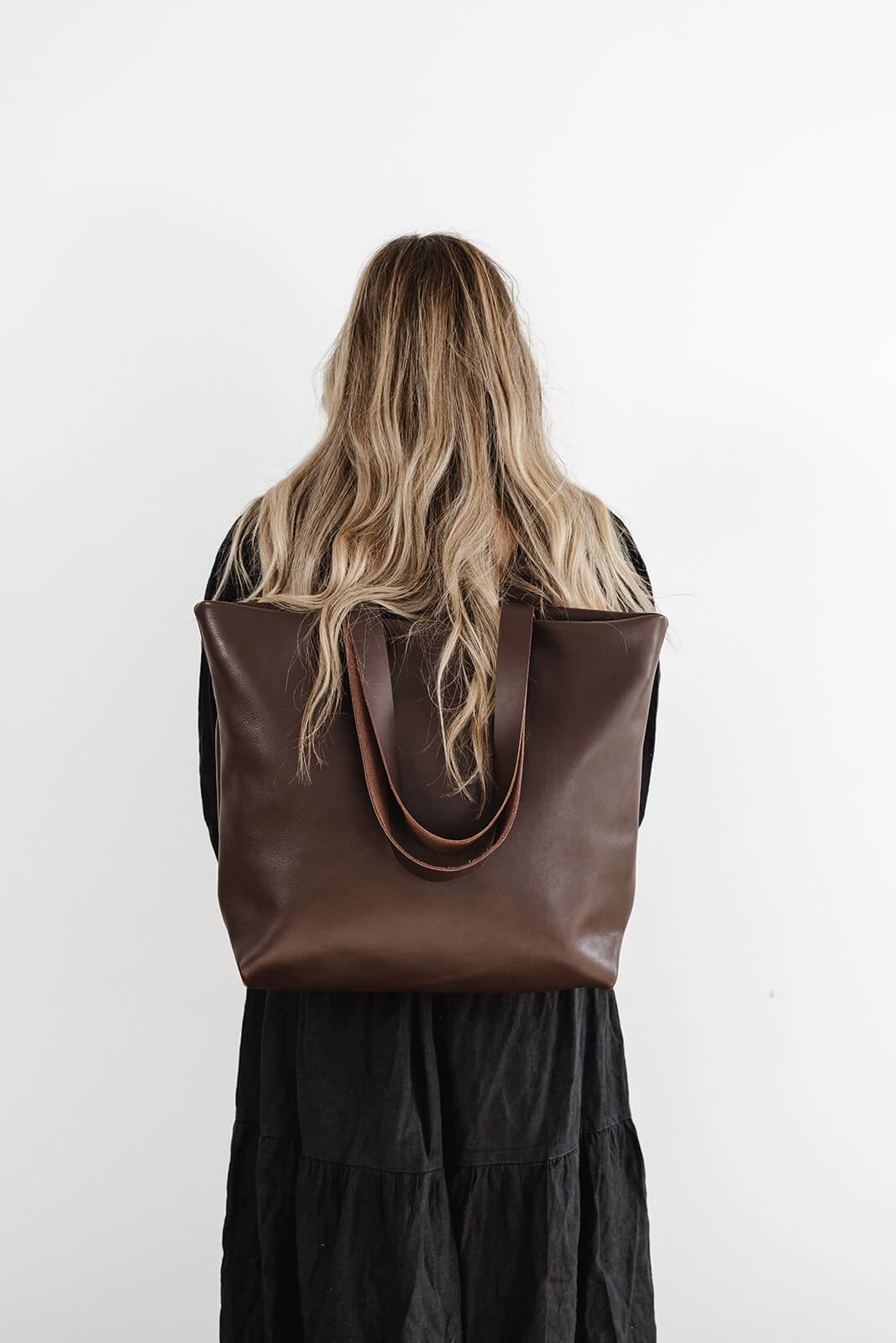 Product pic of the Chocolate Brown Leather Backpack & Tote by Ella Jackson. The backpack is being worn by a woman with a black dress and long sandy coloured hair with a white background