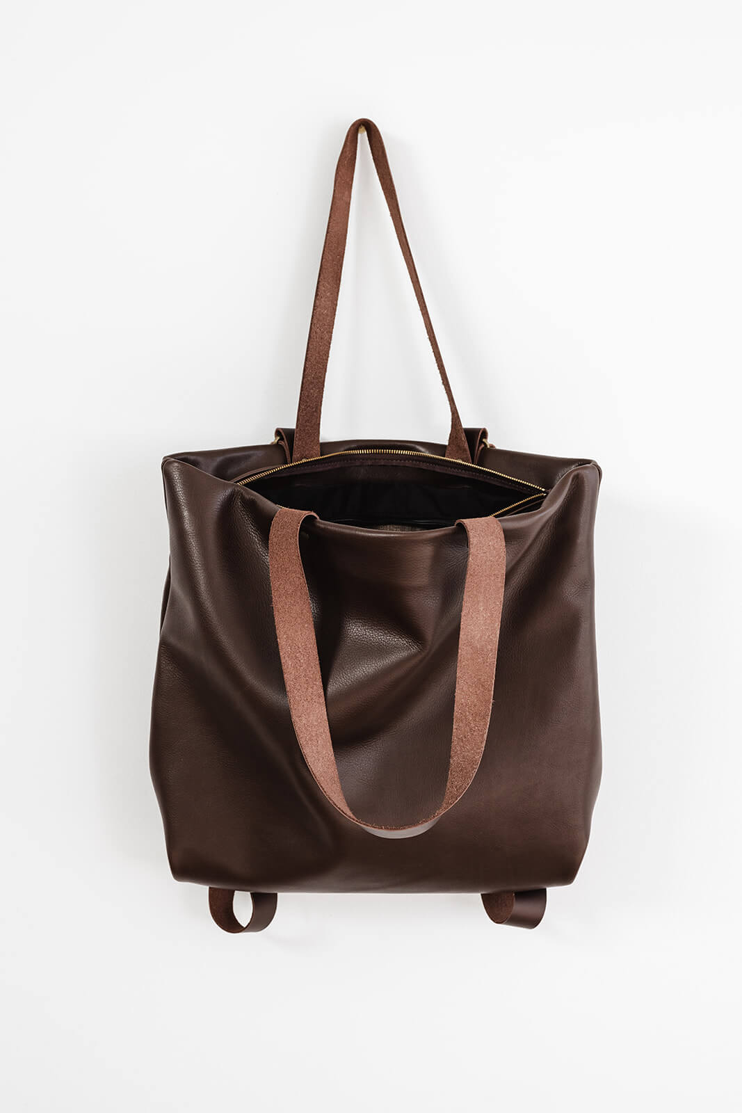 Product pic of the Ella Jackson Chocolate Brown Leather Backpack & Tote. The bag is hanging as a tote on a white background with the zip undone to reveal the black lining