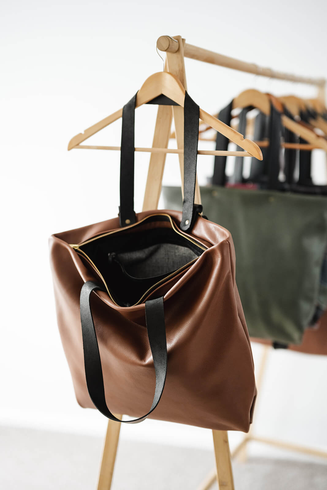 Tan Leather Backpack & Tote in Ella Jackson brand hanging on timber clothes rack as a tote and showing open bag, black straps, gold zip and internal pocket with white and black commercial fabric.