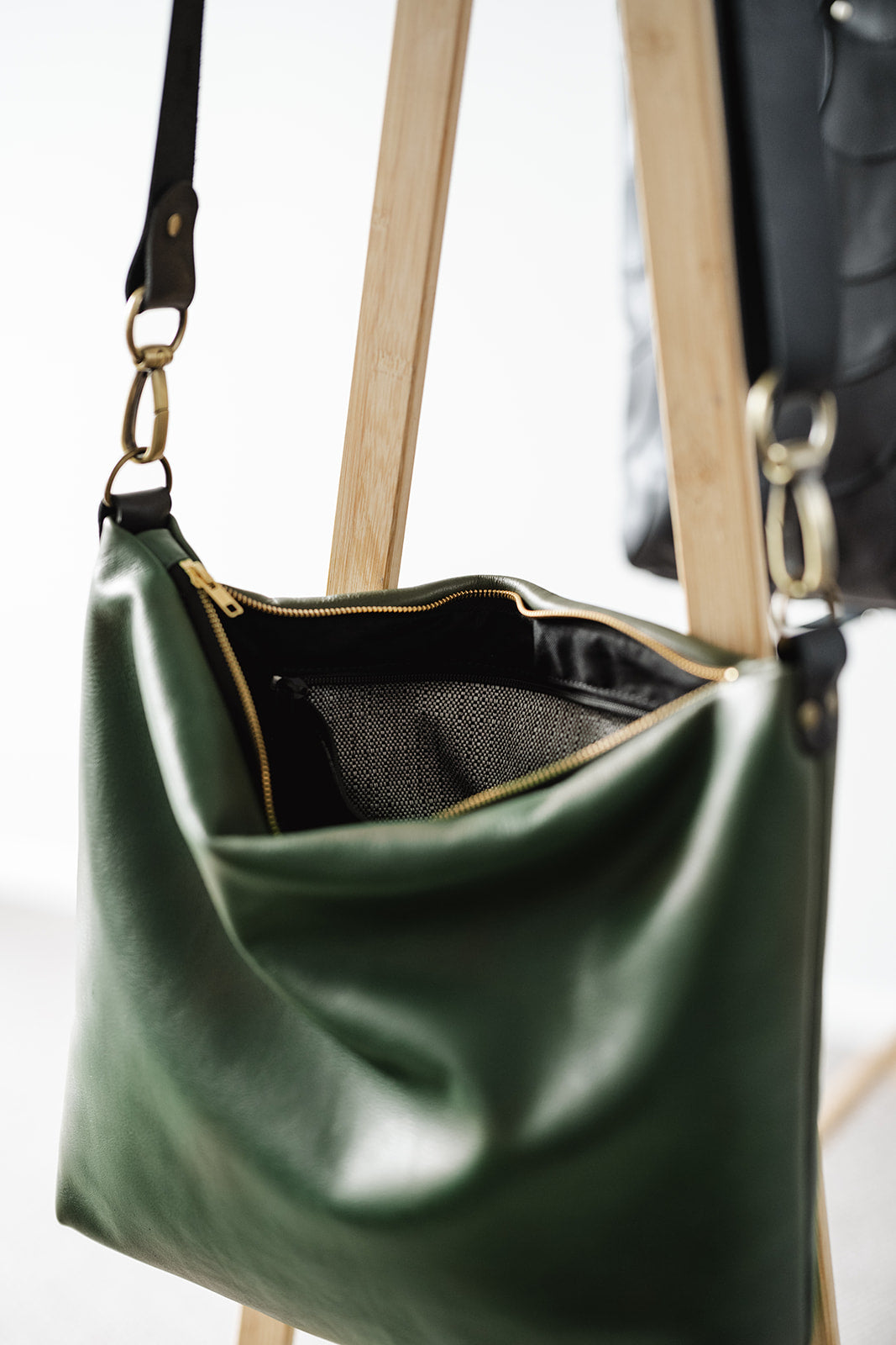 Moss Green Leather Carryall bag in Ella Jackson brand hanging on timber clothes rack showing open bag, strap, gold zip and internal pocket with white and black commercial fabric