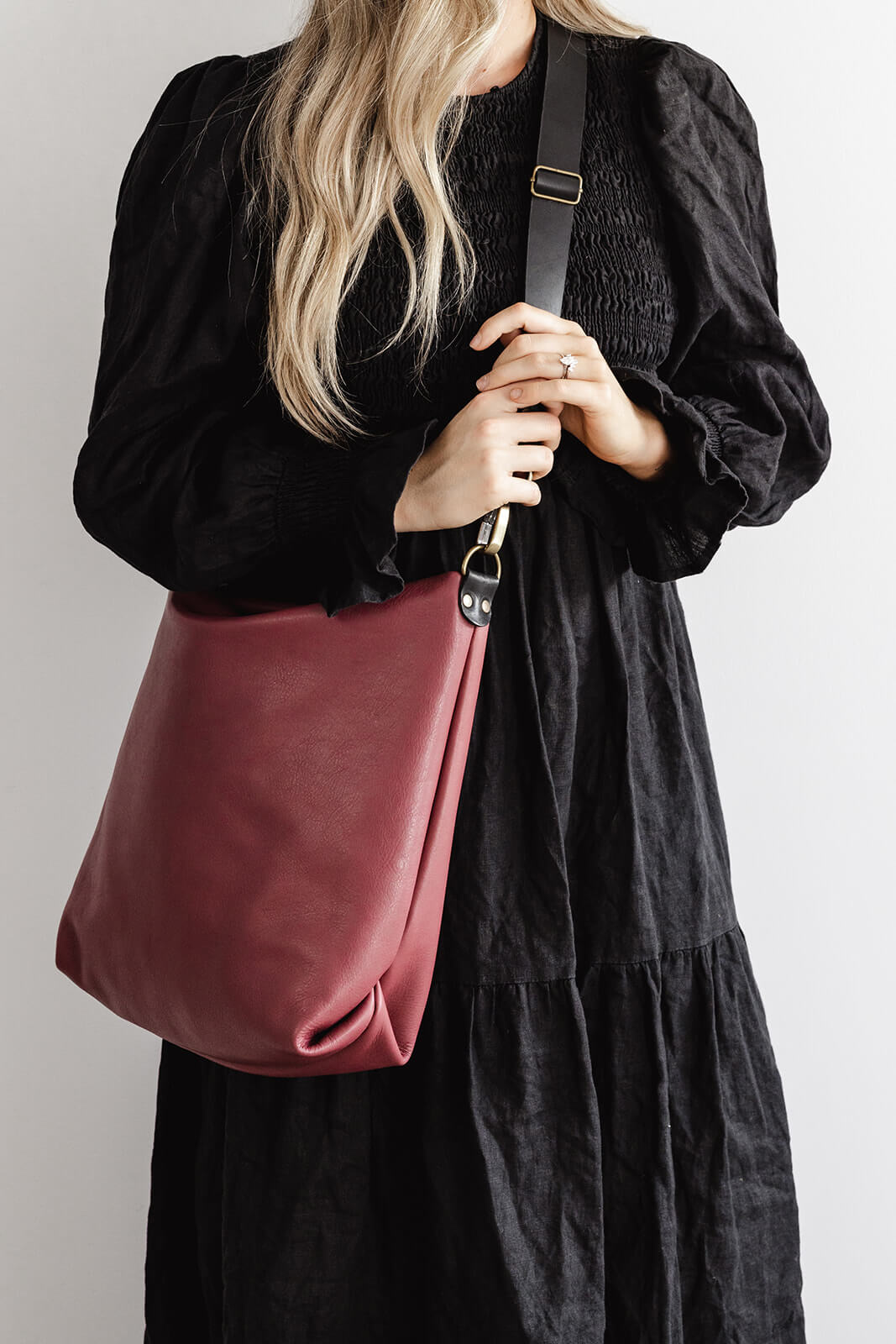 Product shot of the Cherry Leather Carryall by Ella Jackson. The bag is being worn by a woman in a long black dress against a white background
