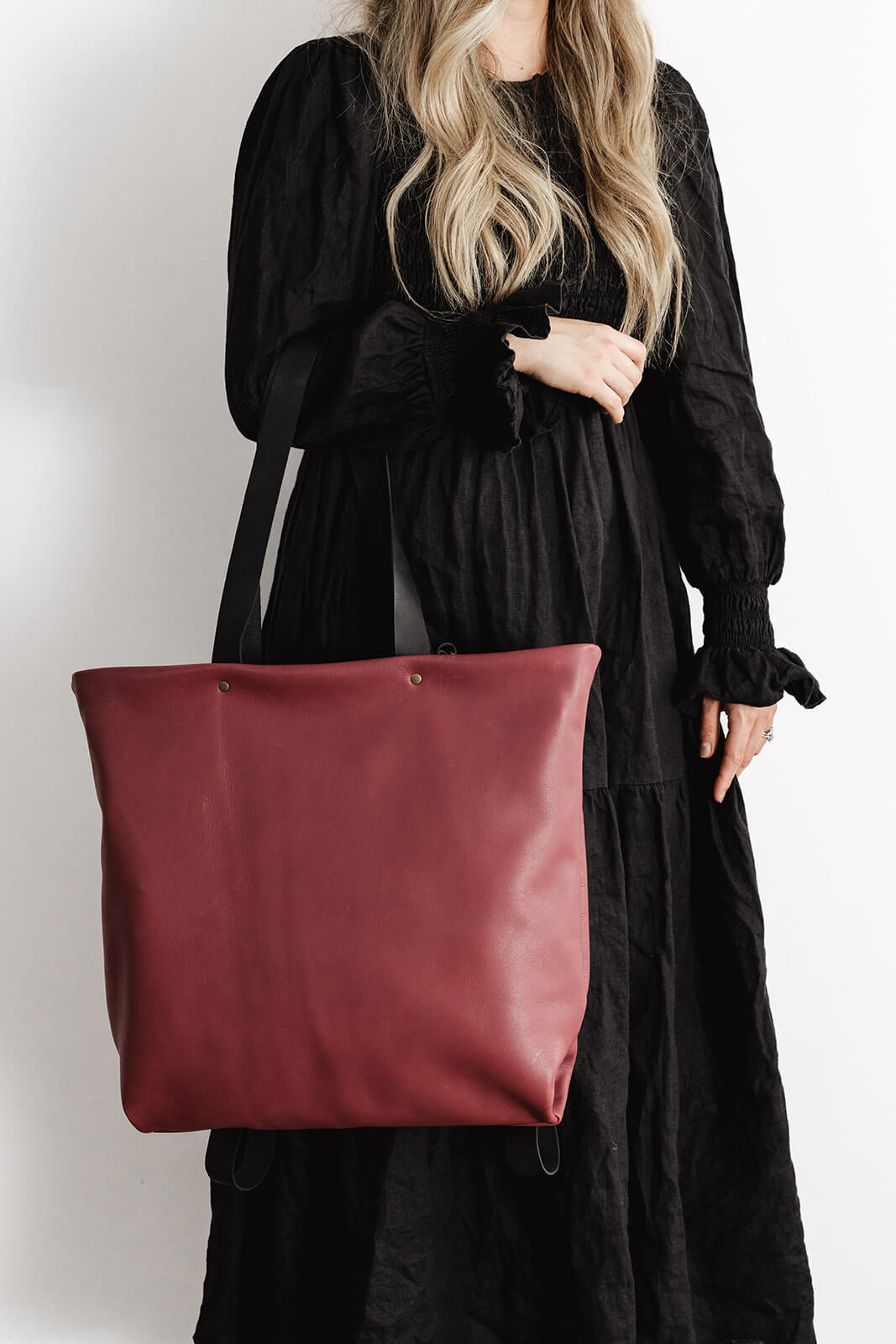 Product pic the Ella Jackson Cherry Leather Backpack & Tote. The bag is being worn as a tote on the elbow of a woman in a long black dress in front of a white background