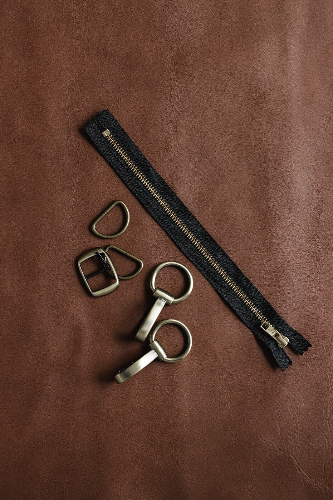 Hands on tan leather showing black and gold ykk zip and antique hardware for Ella Jackson brand