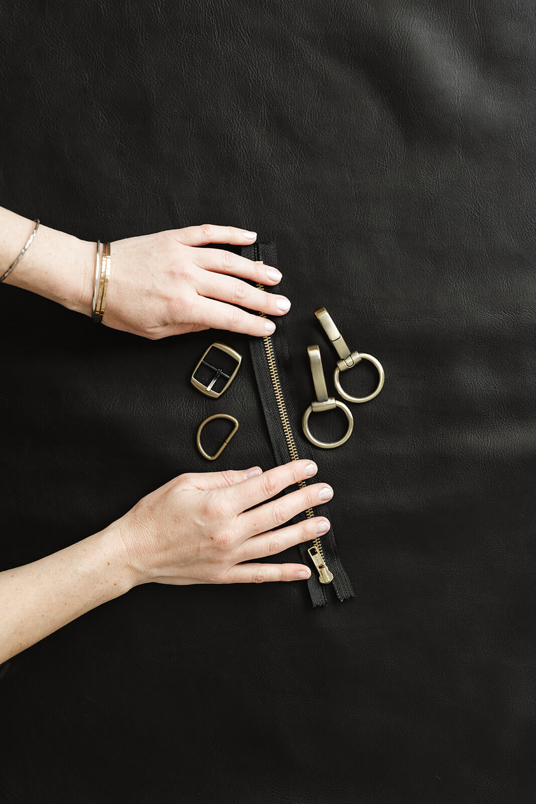 Hands on black leather showing black and gold ykk zip and antique hardware for Ella Jackson brand